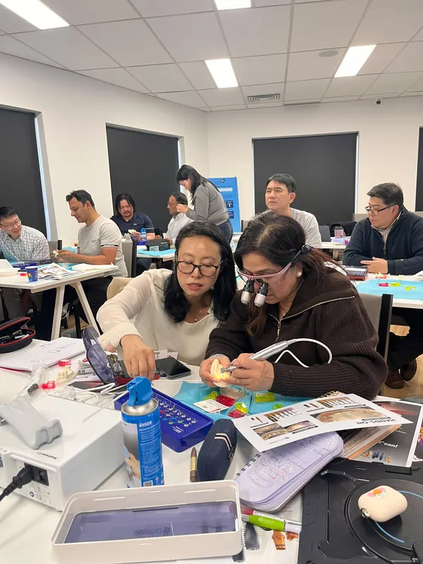 A dentist wearing magnifying loupes places an implant in a training model while a course tutor points to the next drill in the kit