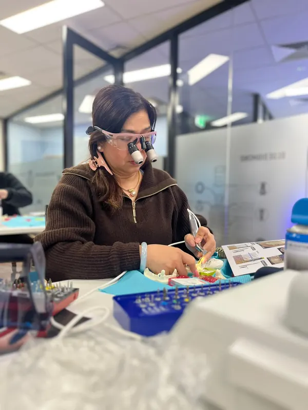 A dentist wearing magnifying loupes uses an implant handpiece on a training model