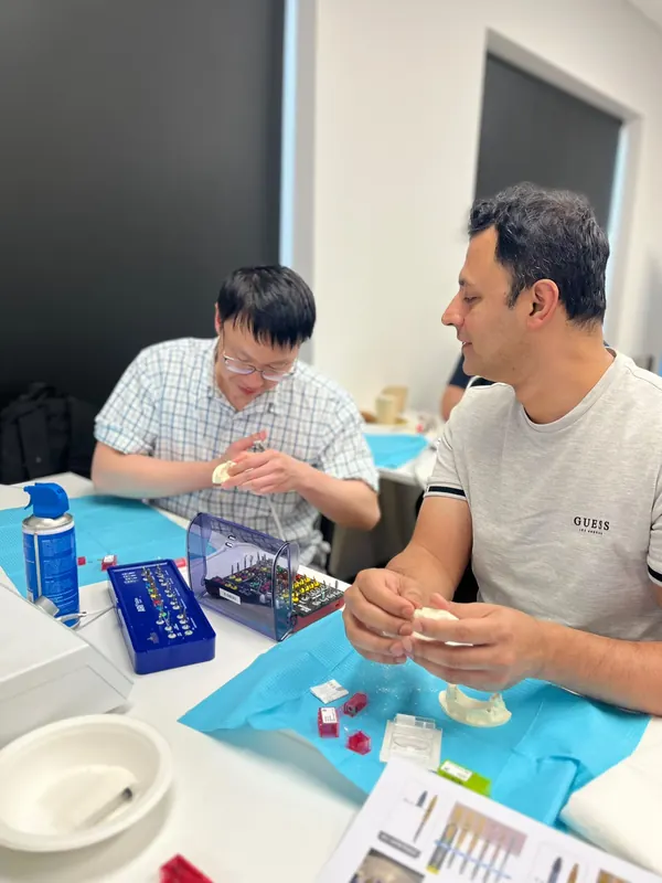 Two dentists working side by side on training models with surgical kits open in front of them