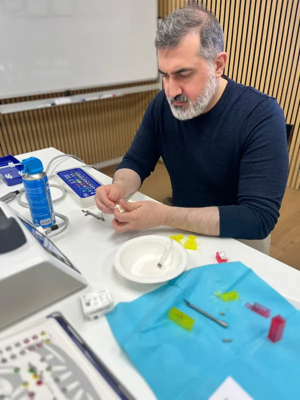 A dentist seated at a workstation fits a component to a training model